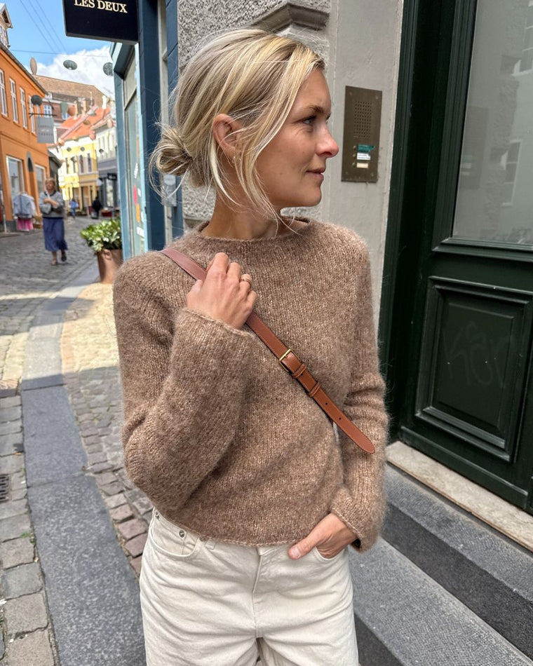 Detaljebillede af ærmet på brun Ivy Sweater liggende i sandet